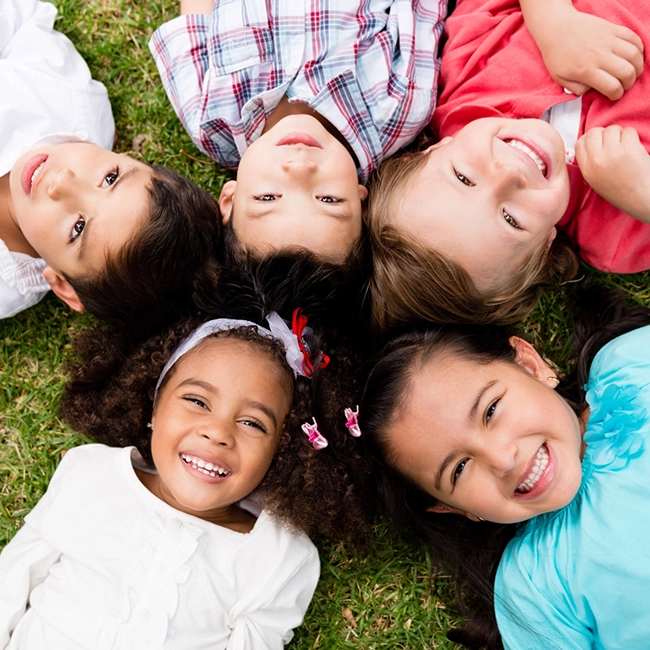 Group of children from diverse backgrounds, ages 1-5 laying on green grass